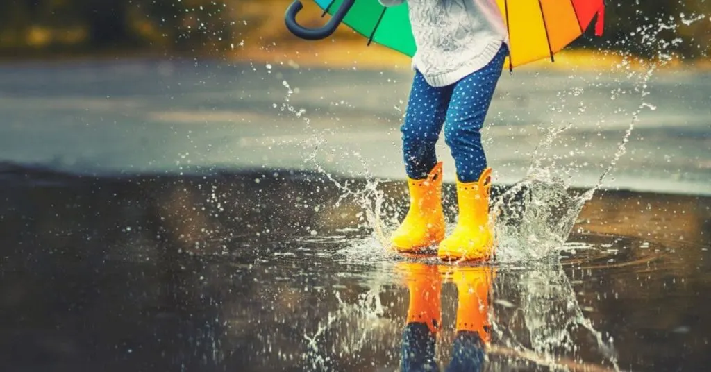 A girl having fun jumping in a puddle of water.