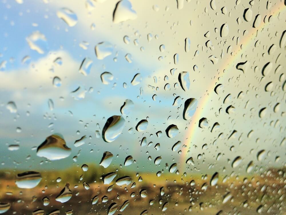 Regentropfen auf einer Scheibe mit Regenbogen im Hintergrund
