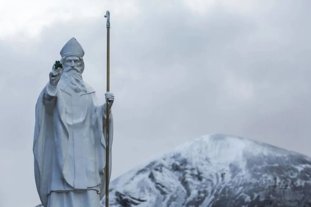 Die Statue des Heiligen Patrick am Fuß des Croagh Patrick mit dem schneebedeckten Gipfel im Hintergrund.