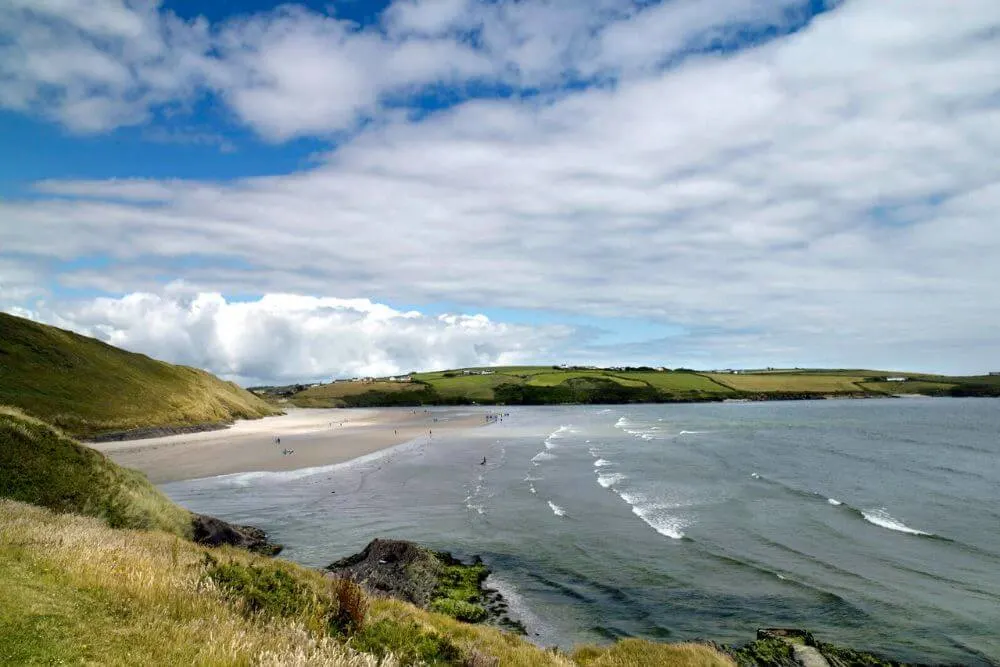 A scenic view of Inchydoney East Beach with people enjoying the sand and having fun in the waves.