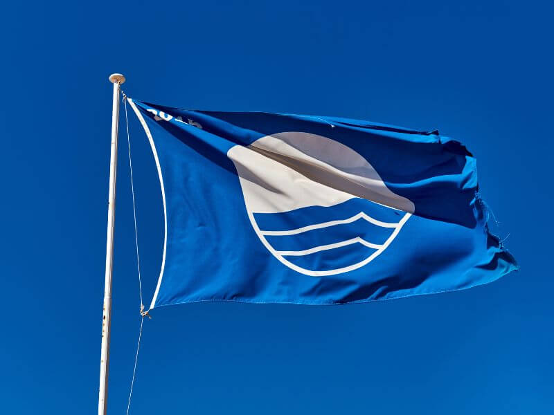 Beach Award Blue Flag flying on a flagpoll against a blue sky.