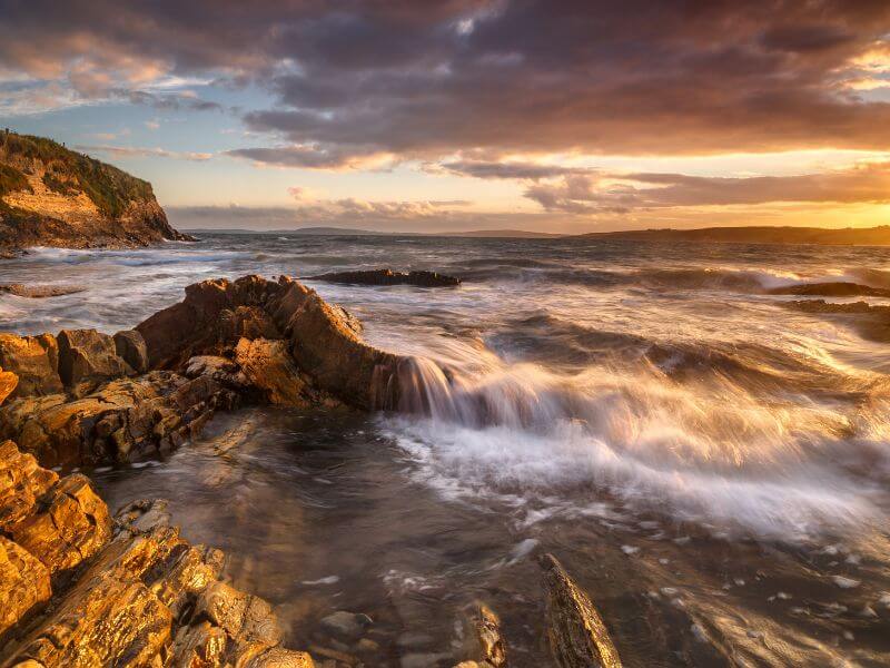 Waves pouring over the rocks at Garretstown Beach in the golden light of sunset.