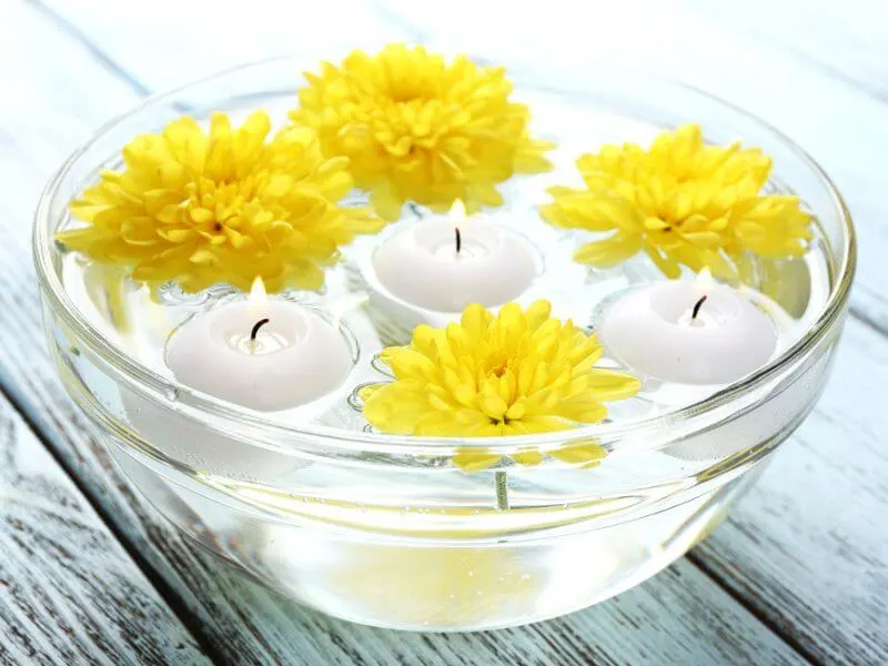 Bowl of water with yellow flowers and candles. 