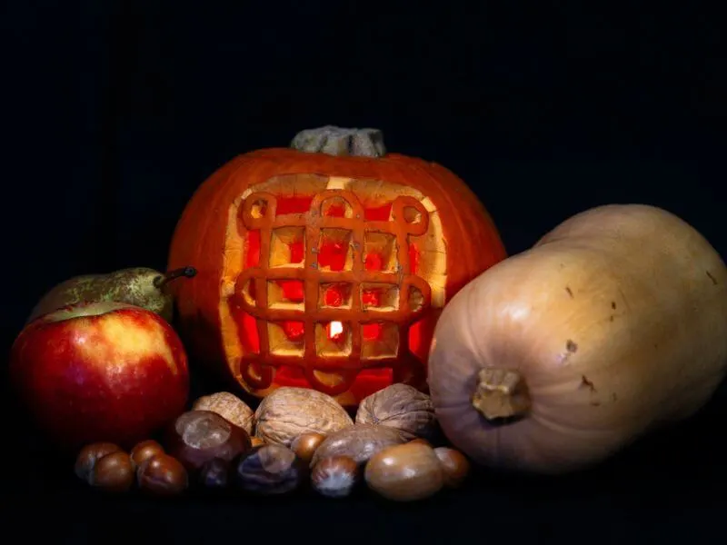 A carved pumpkin and other harvest season produce. 