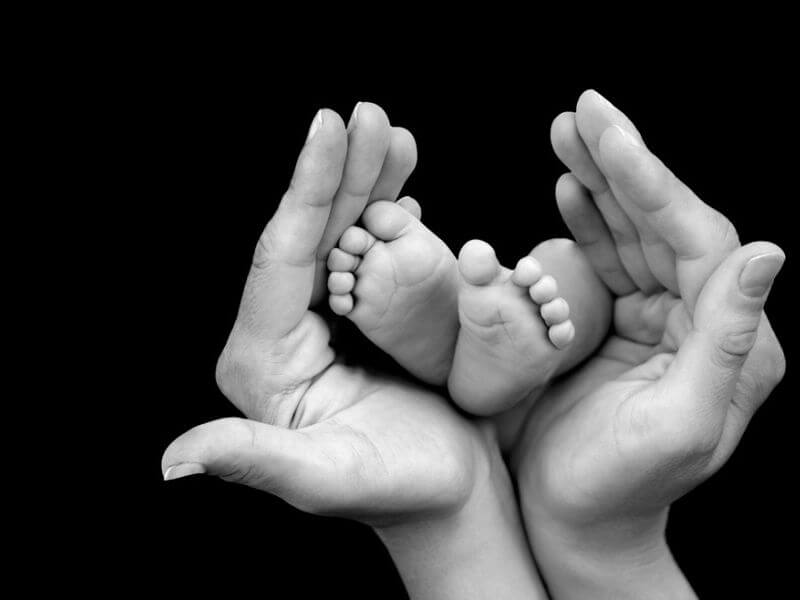 Neugeborene Füße in den Händen eines Elternteils.